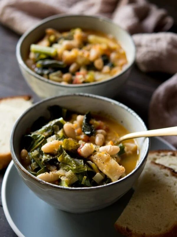 Tuscan vegetable soup in a bowl with bread in background
