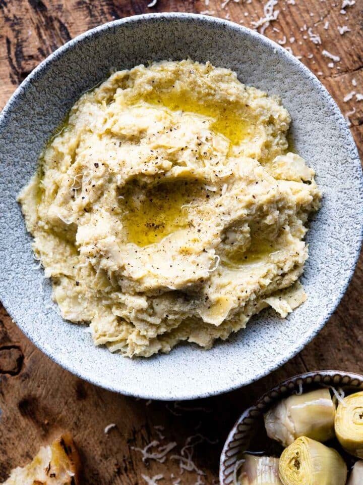 An overhead shot of artichoke pesto in a bowl sitting on a wodden board.