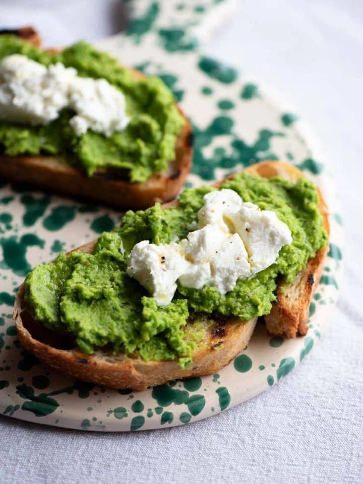 A close up of bruschetta topped with pea pesto and goat cheese on a ceramic serving board.