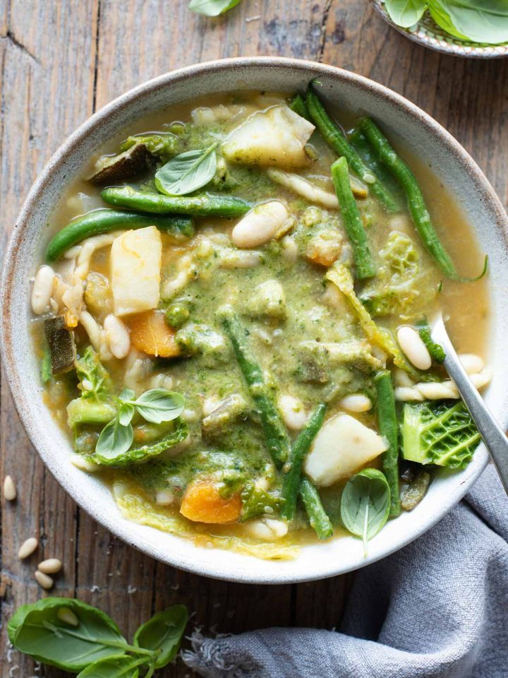An overhead shot of a bowl of Ligurian minestrone with lots of vegetables and basil pesto sitting on a wooden background