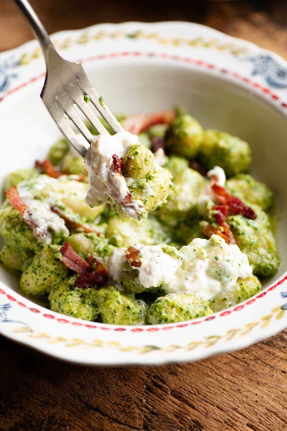 A close up of a fork picking up some arugula pesto gnocchi.