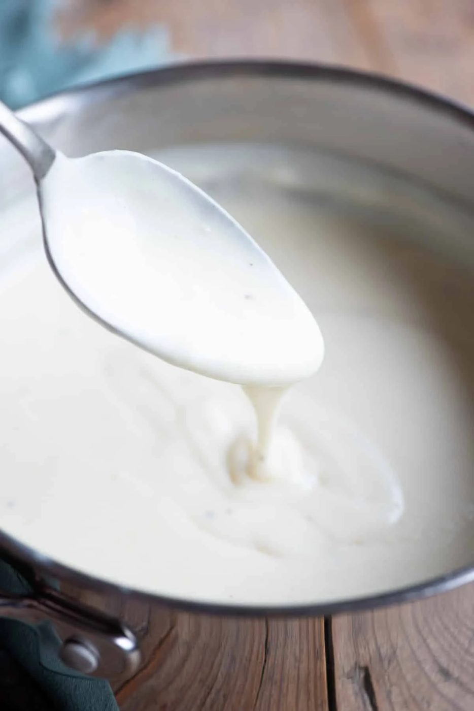 A close up of Italian Besciamella sauce in a pot with some dripping off a spoon.