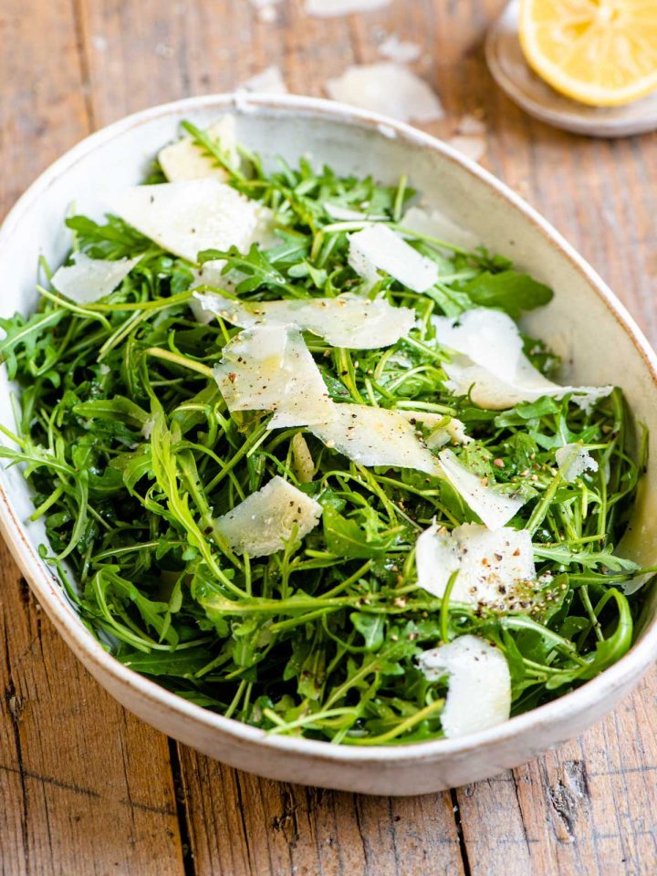An arugula salad in a large serving bowl with shavings of parmesan