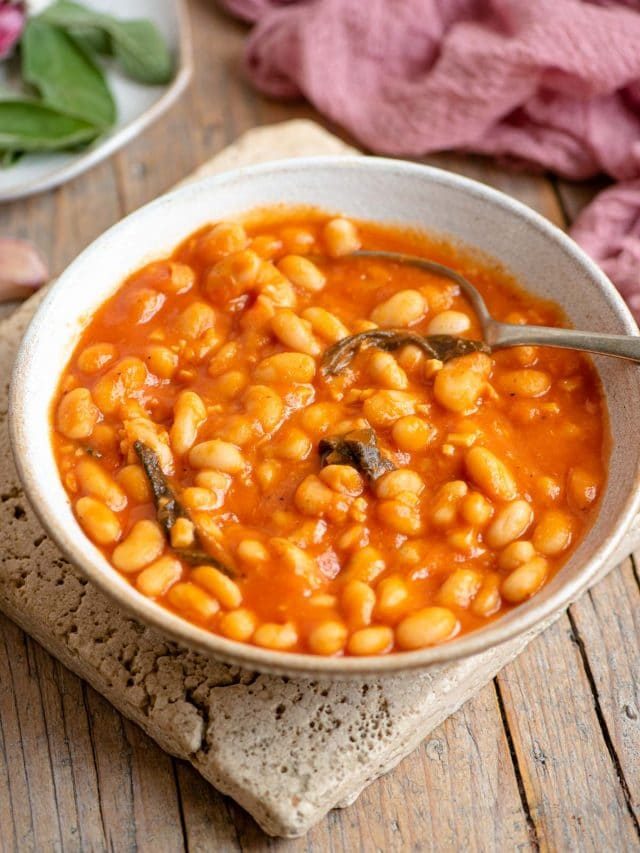 A bowl of cannellini bean in tomato sauce with sage sitting on a wooden surface