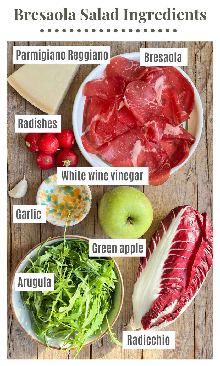 All the ingredients to make a bresaola salad on a wooden surface.
