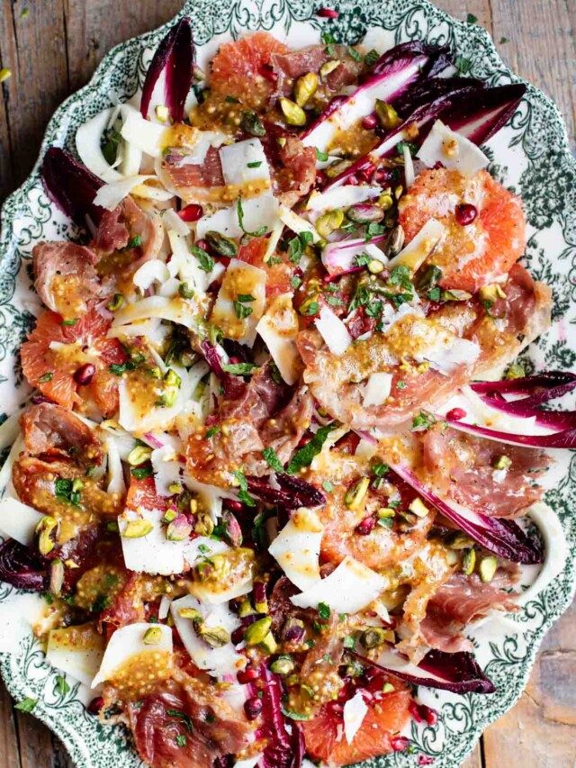 A green serving platter with a festive, colourful salad filled with blood orange, raddichio, fennel, pomegranate, pistachios and prosciutto.