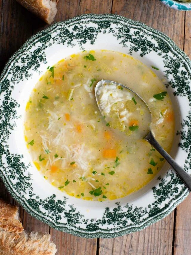 An overhead shot of an Italian rice soup in a green and white bowl with a spoon inside.