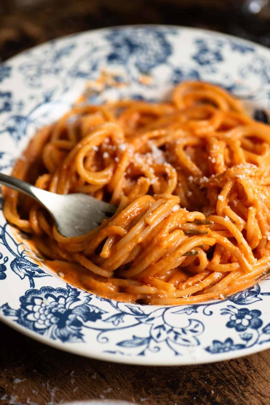 A close up of spaghetti with creamy roasted red pepper sauce rolled around a fork.