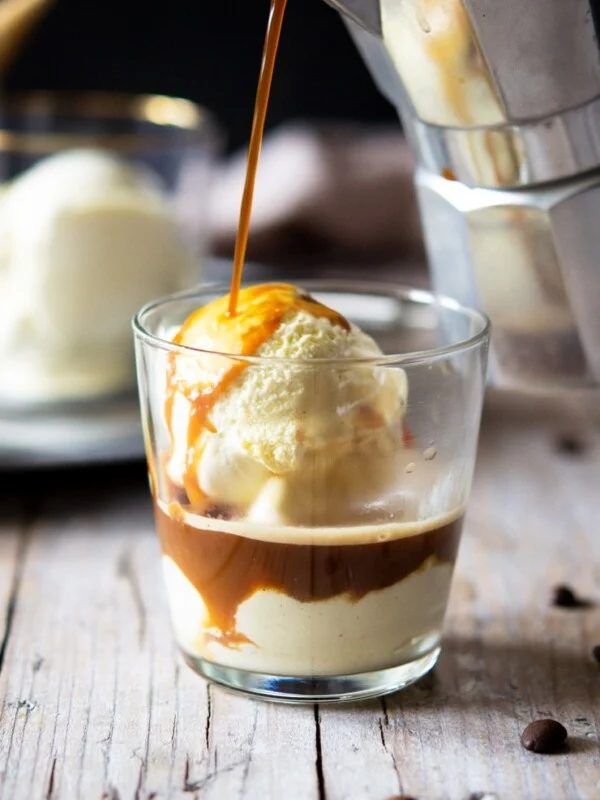 A photo of coffee getting poured over ice cream in a glass to make an affogato