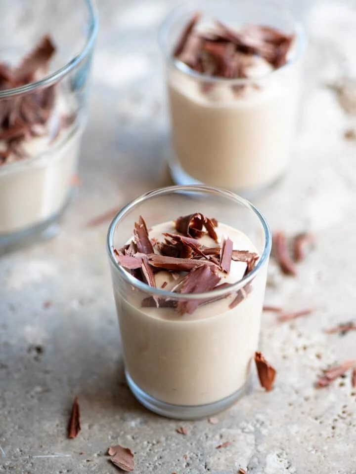 A close up of Ricotta al Caffe (ricotta and coffee) in small glasses topped with dark chocolate. The background is stone.