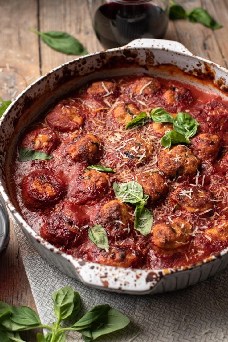 A close up of baked chicken meatballs in a baking dish with basil and parmesan on top