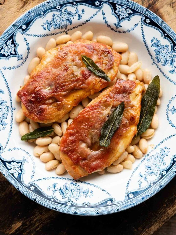 Two pieces of chicken saltimbocca on a plate on top of cannellini beans.