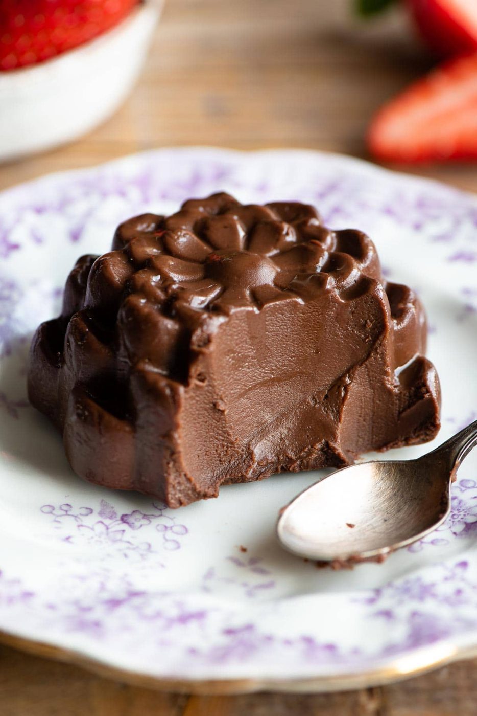 A close up of a chocolate budino with a bite out sitting on a small white plate