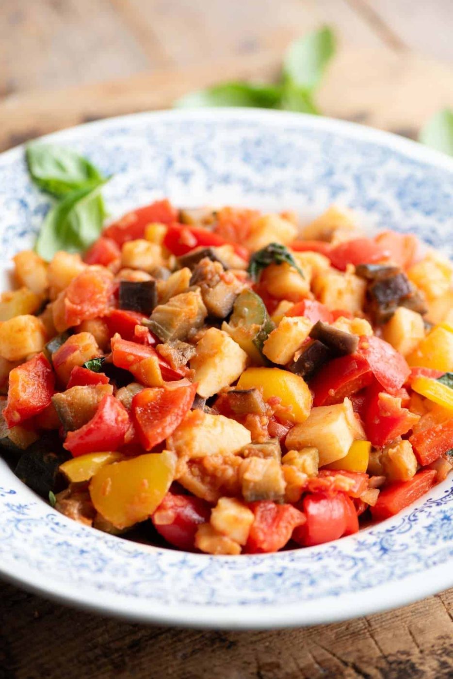 A side shot of Ciambotta vegetable stew in a blue and white bowl sitting on a wooden board.