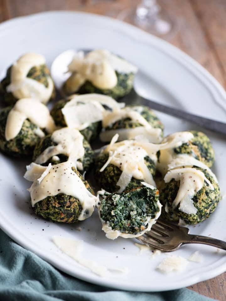 Spinach balls on a white serving plate with parmesan cream. One is cut open on a fork.