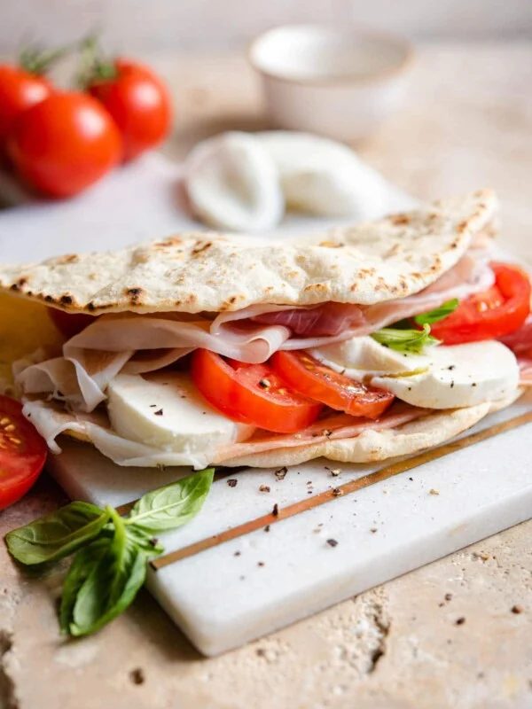 A Piadina flatbread stiffed with tomato, mozzarella and prosciutto on a marble board