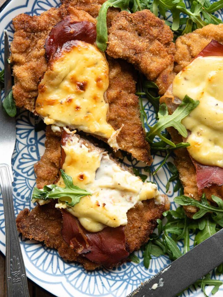 A close up of a veal cutlet cut in half with parmesan cream and prosciutto on top