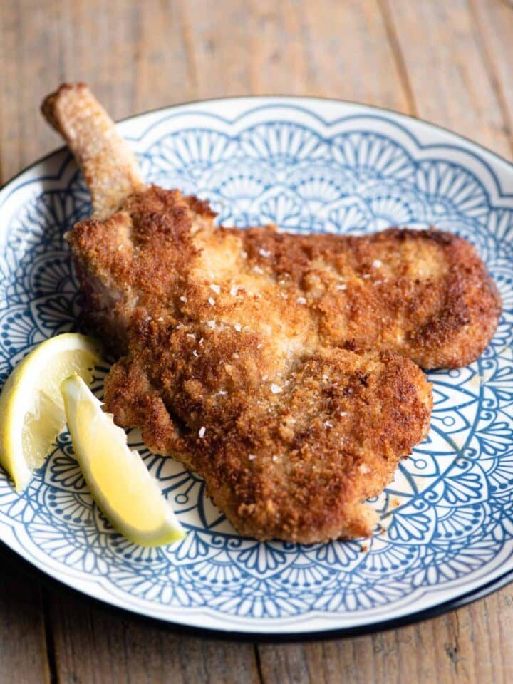 Veal Milanese (veal cutlet) on a blue plate with lemon wedges at the side.