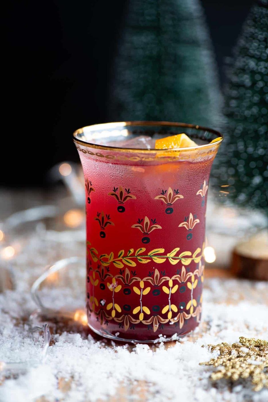 A close up side shot of a Cranberry and Prosecco cocktail sitting on a wooden table with snow all around.