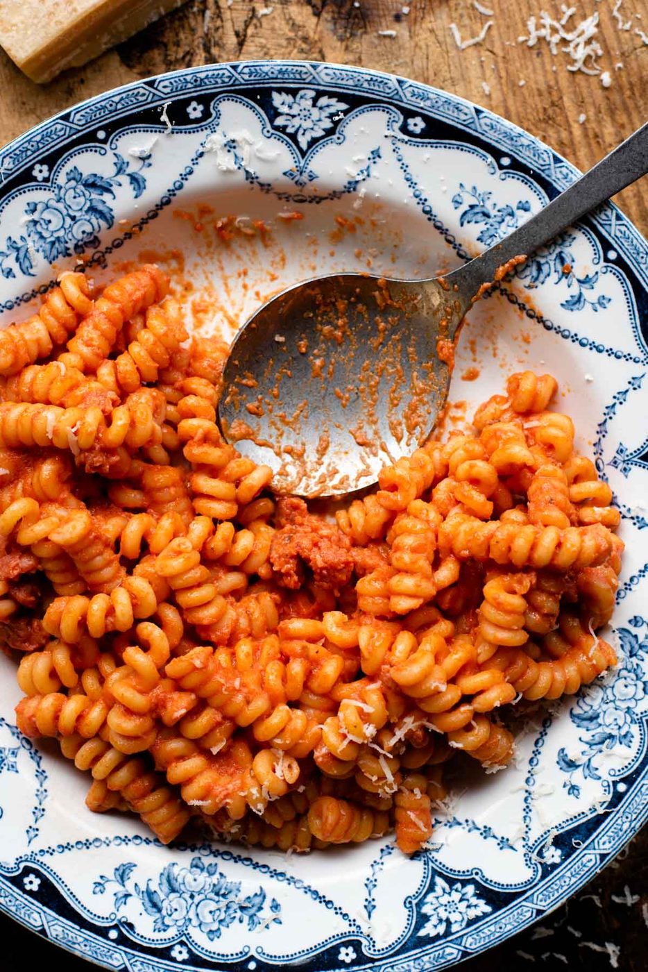 An overhead shot of Creamy Tomato Pasta and Italian Sausage in a blue patterned bowl with a serving spoon at the side.