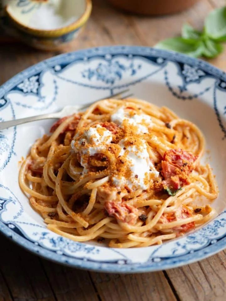 Roasted cherry tomato spaghetti in a blue bowl sitting on a wooden background.
