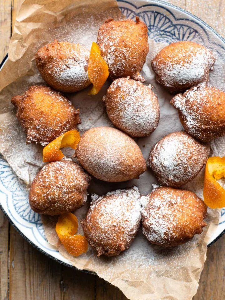An overhead shot of small ricotta doughnuts on a plate dusted with powdered sugar