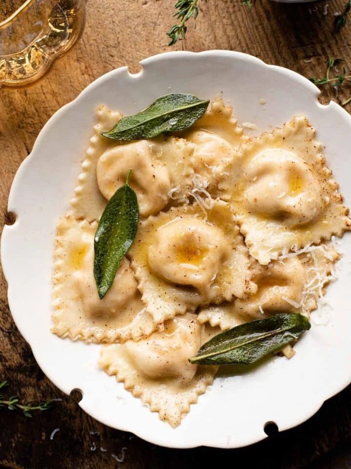 An overhead shot of butternut squash ravioli in a white bowl sitting on a wooden serving board.