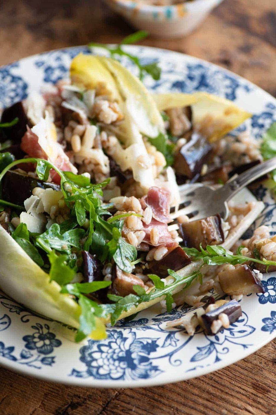 A close up of a eggplant and farro salad made with bitter greens and pine nuts.