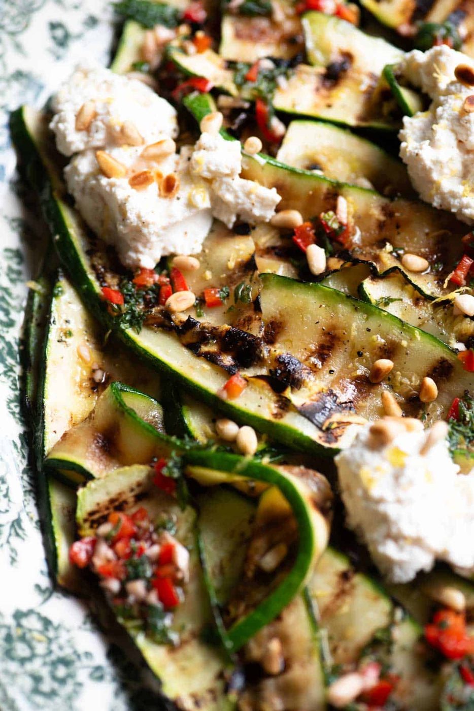 A close up side shot of grilled zucchini on a platter with mint, chilli, garlic and ricotta.