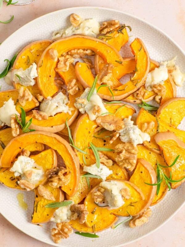 An overhead shot of roasted butternut squash on a serving plate with gorgonzola and walnuts