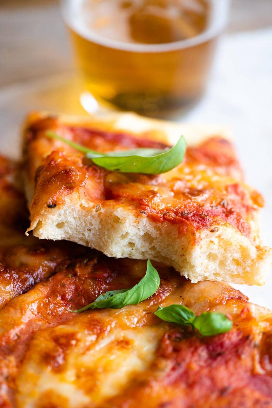 A close up of a slice of focaccia pizza with a bite out so you can see the fluffy texture