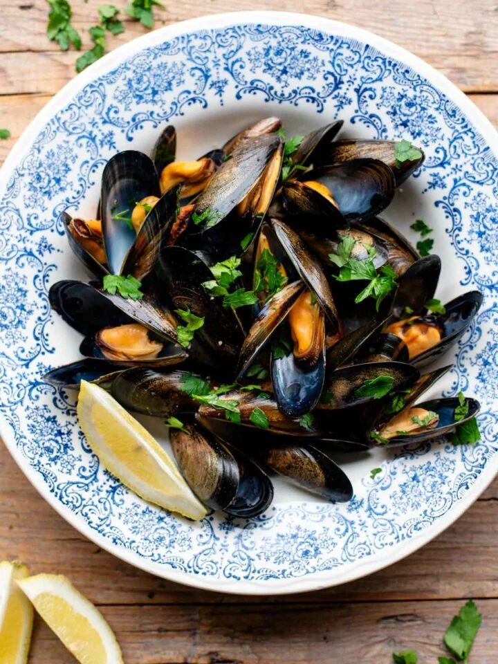 An overhead shot of peppered mussels in a blue bowl with fresh parsley and lemon.