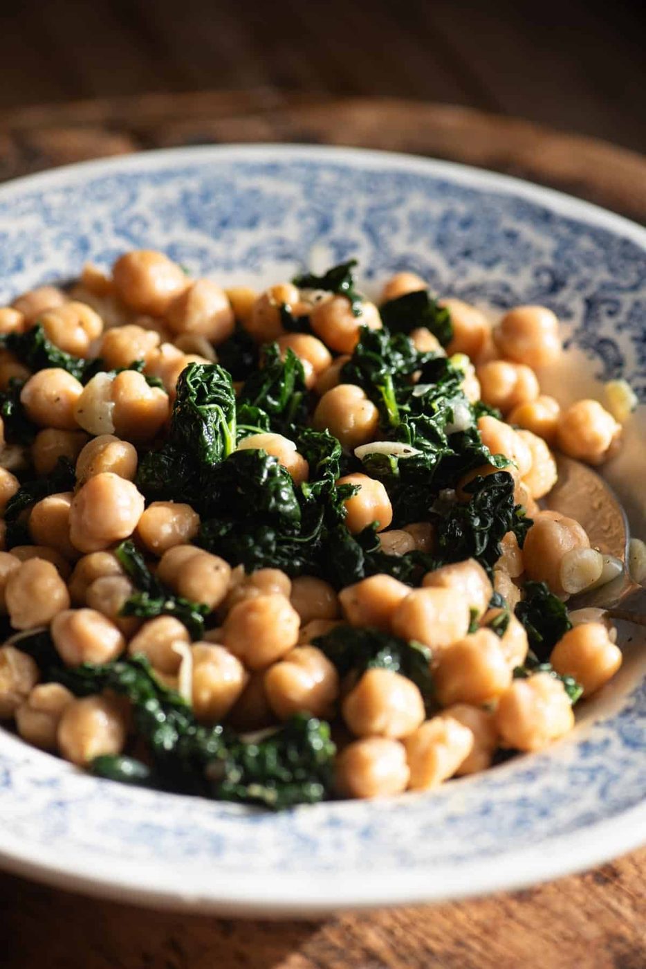 A close up of chickpeas and cavolo nero in a blue and white vintage style bowl sitting on a rustic wooden surface.