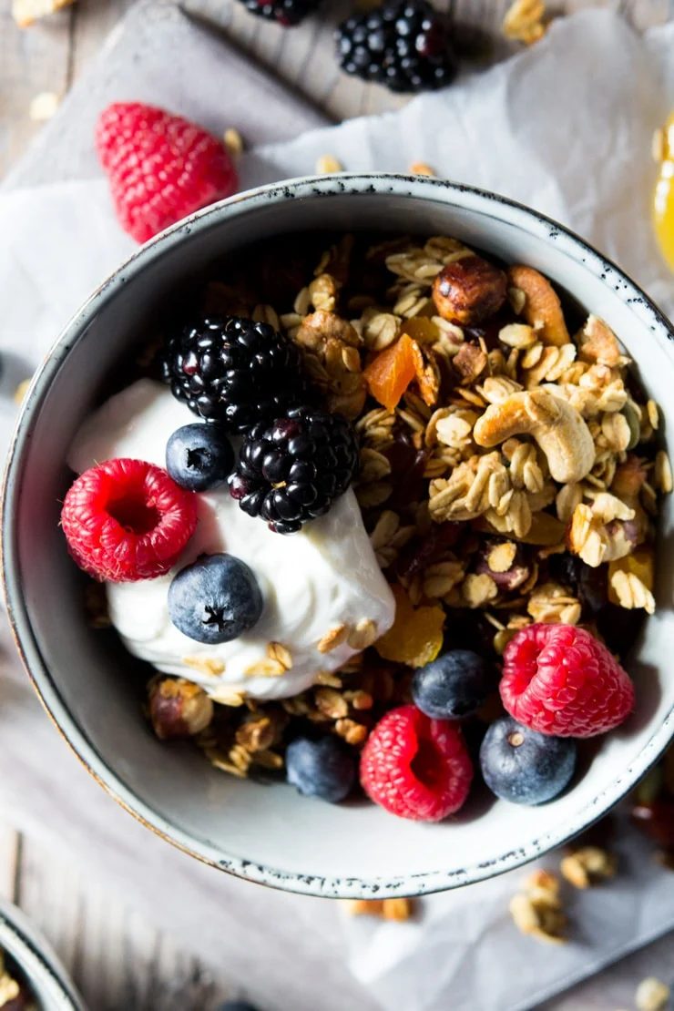 A close up of healthy granola in a blue bowl topped with yogurt and berries