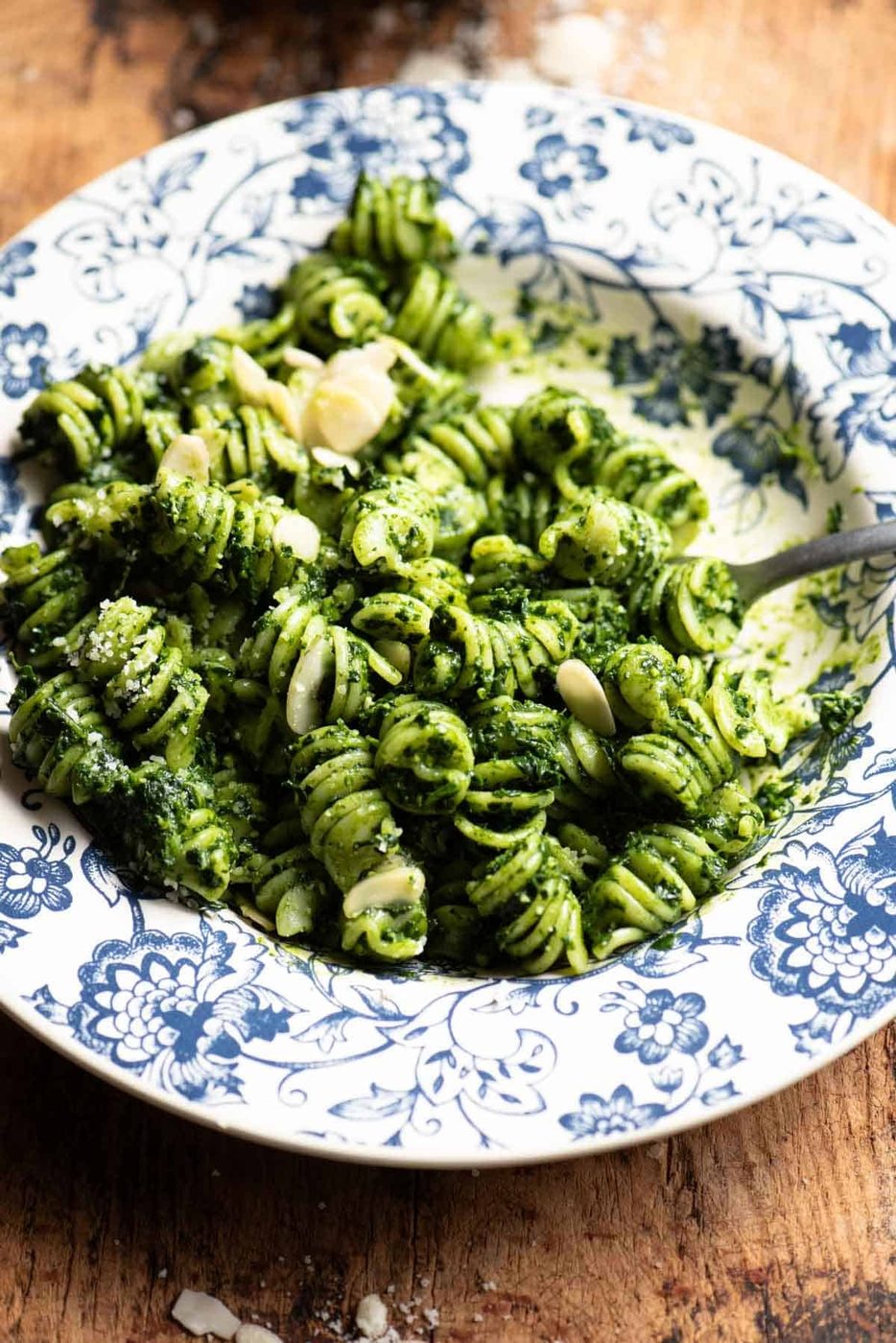 A close up of kale pesto pasta topped with flaked almonds in a blue floral bowl.