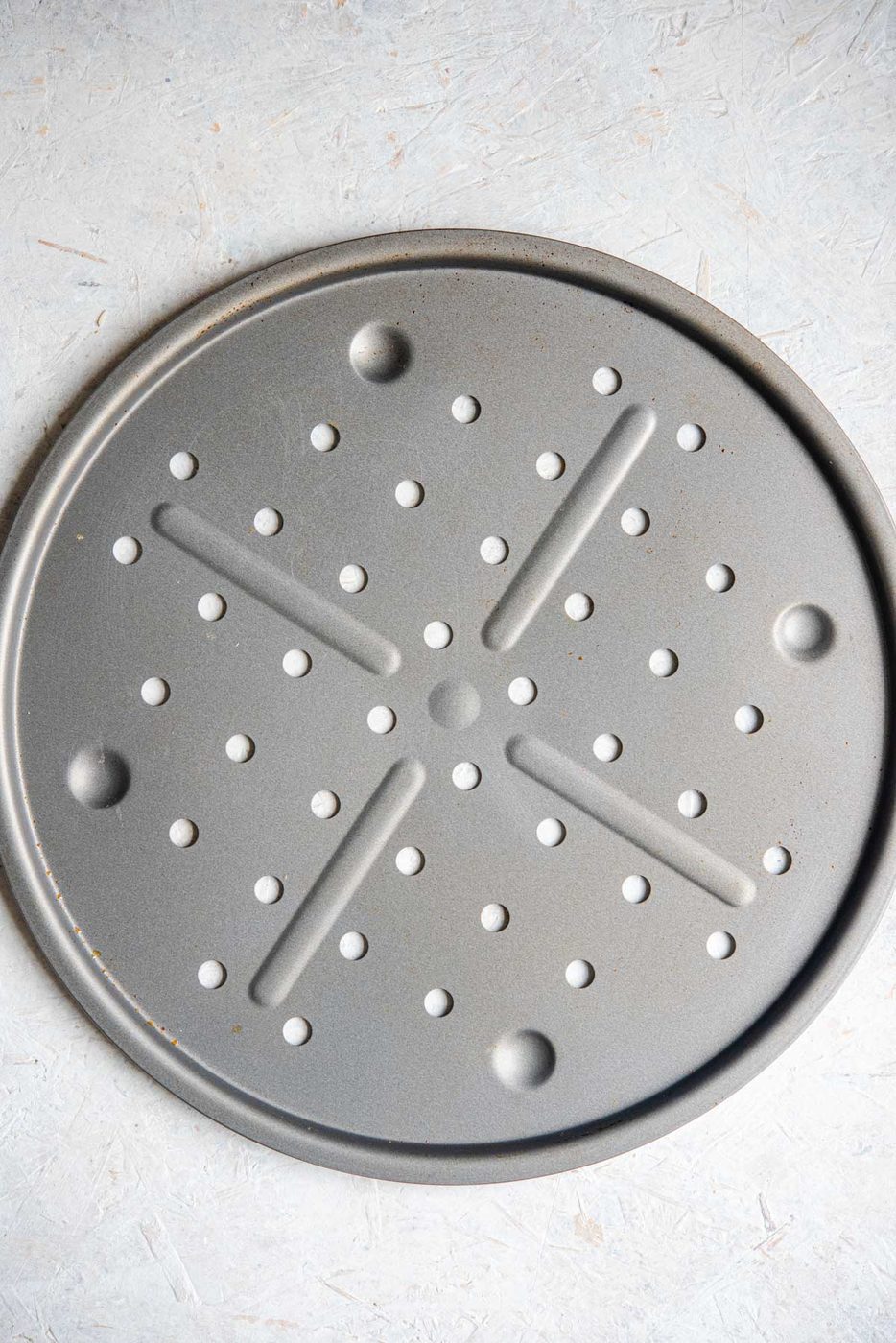 An overhead shot of a circular pizza tray with holes