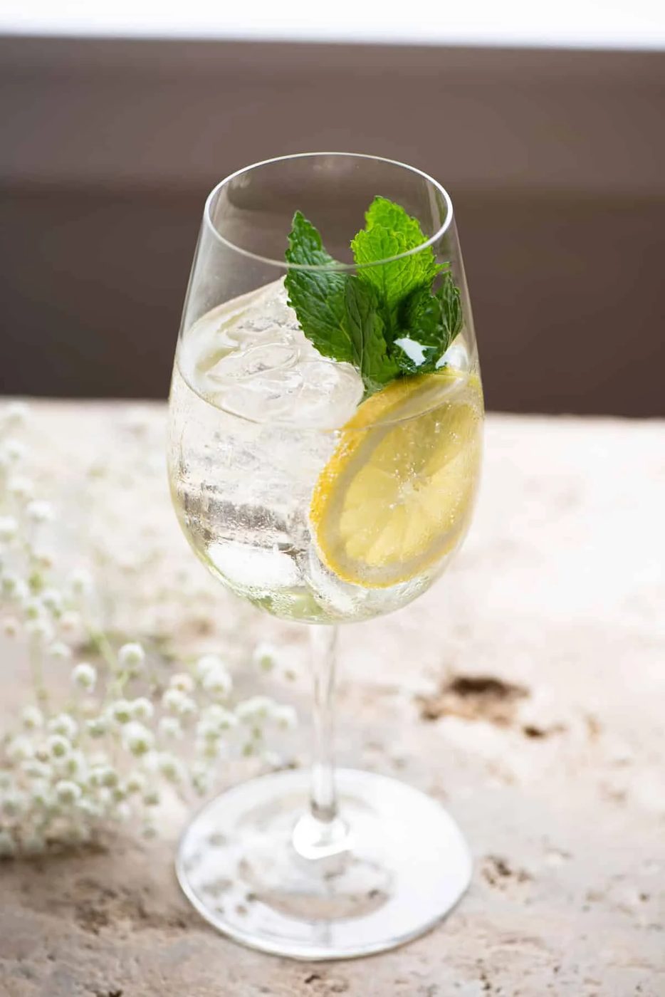 A hugo spritz cocktail on a stone worktop garnished with lemon and mint leaves.