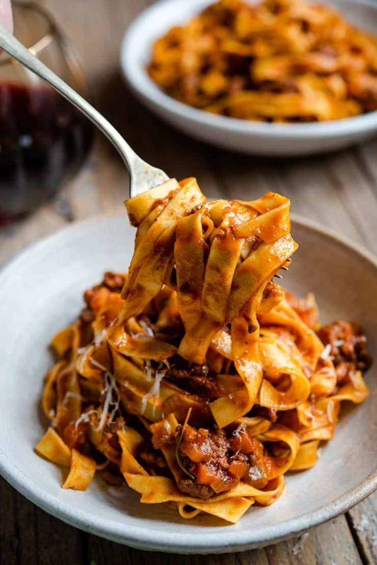 A fork picking up some beef ragu and pasta from a bowl.