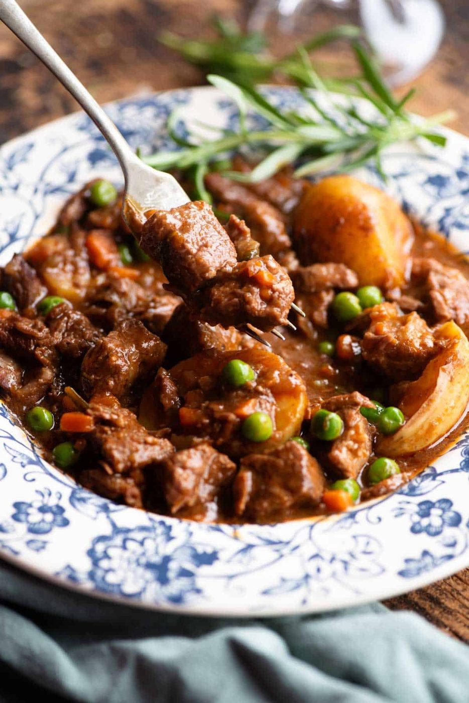 A close up of a fork picking up some beef from a bowl of beef stew.