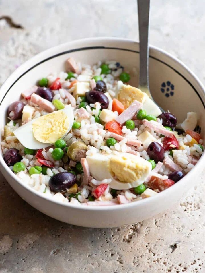 A traditional Italian rice salad in a bowl sitting on a rustic stone work top.