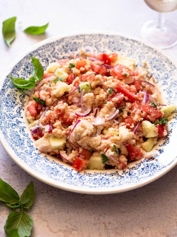 Authentic Tuscan Panzanella Salad in a blue patterned bowl with basil around.