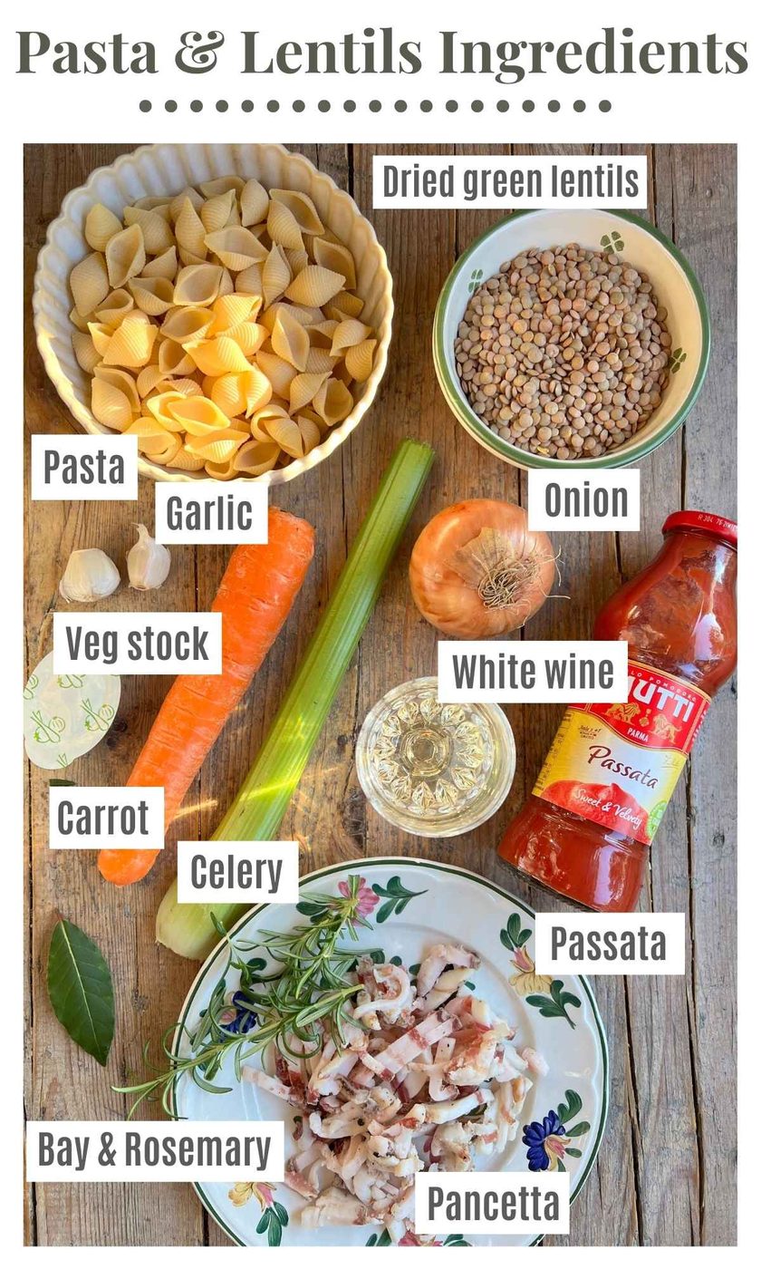 An overhead shot of all the ingredients needed to make pasta and lentils. The ingredients are labelled: pasta, dried green lentils, passata, carrot, celery, onion, bay and rosemary, pancetta, white wine, garlic.