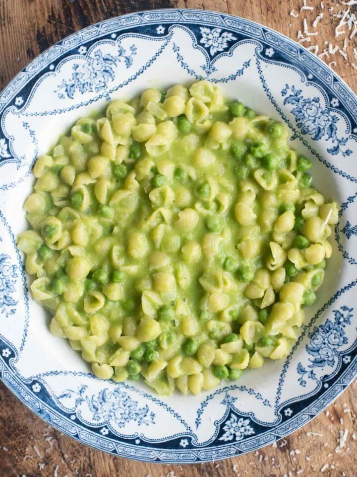 An overhead shot of Pasta and Piselli (peas) in a blue bowl sitting on a wooden surface.