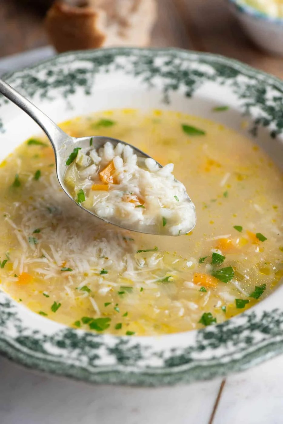 A close up of a spoon picking up a spoonful of Italian rice soup from a green patterned bowl.
