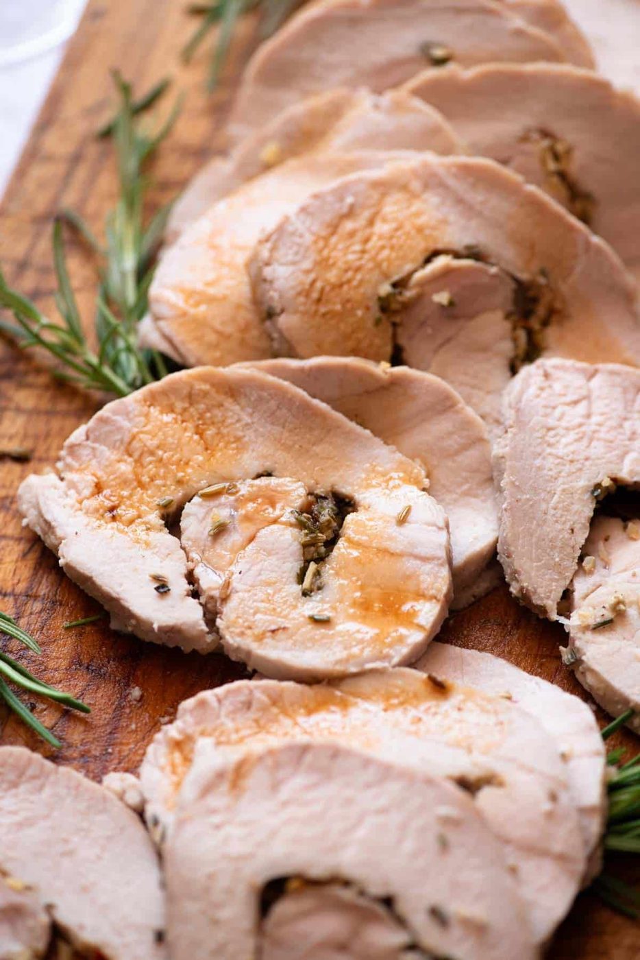 A close up of Italian stuffed pork loin on a wooden board drizzled with gravy.