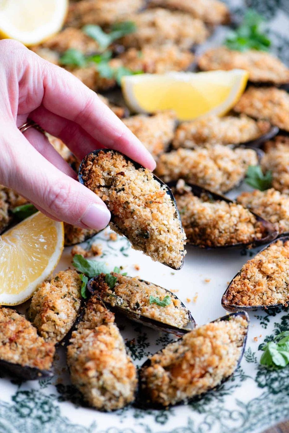 A close up of a hand holding a stuffed mussel over a serving plate.