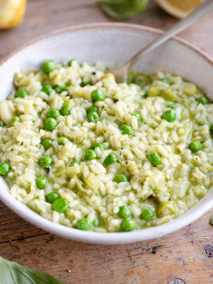 A side shot of a pea and pesto risotto in a bowl in a wooden surface with a fork at the side