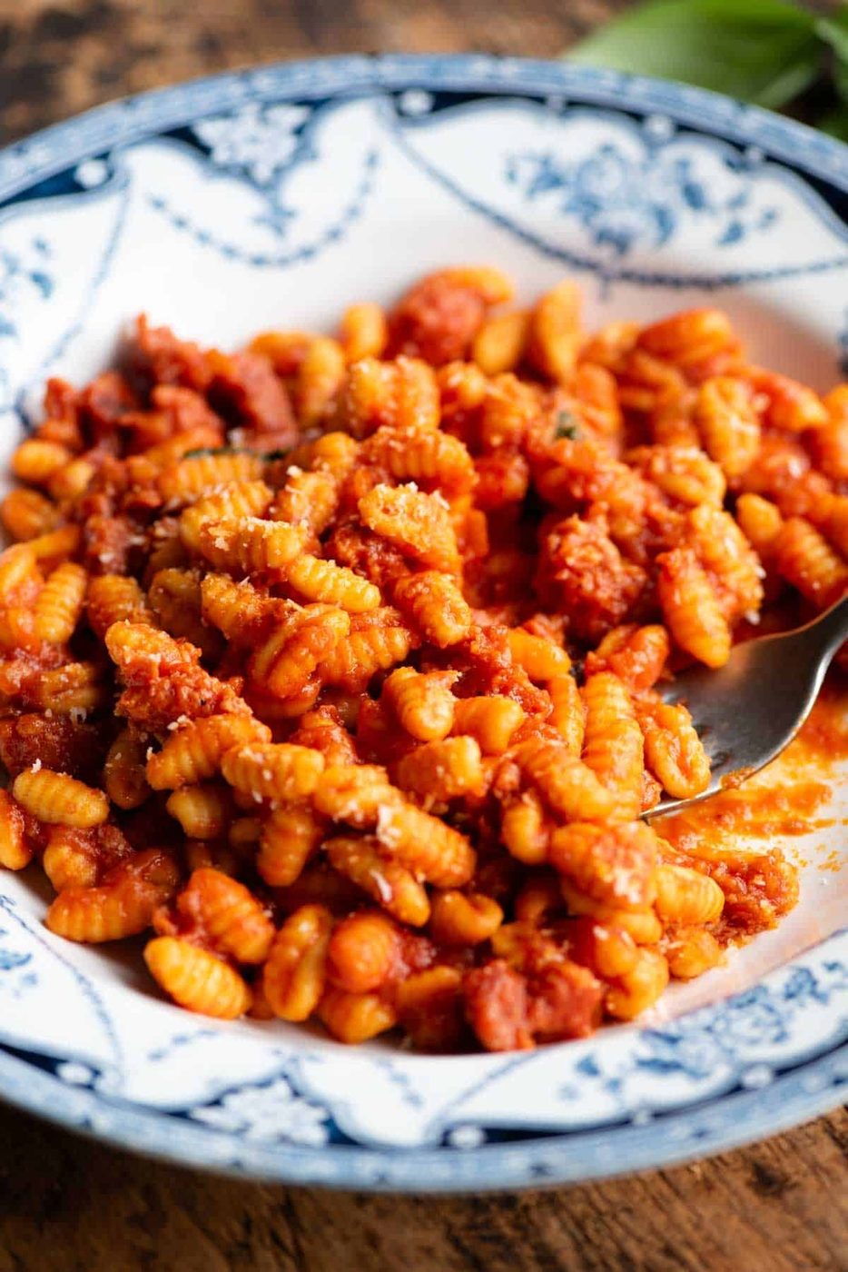 A close up side shot of a Sardinian sausage pasta in a blue and white bowl with a fork.