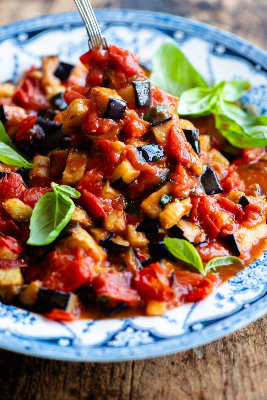 A close up of fried eggplant in tomato sauce in a bowl with fresh basil.