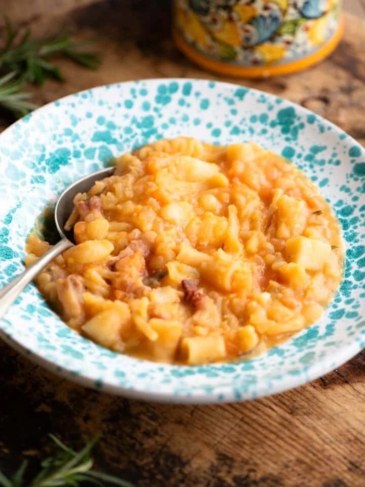 Pasta e Patate (potatoes) in a blue speckled bowl with a spoon sitting on a wooden surface.